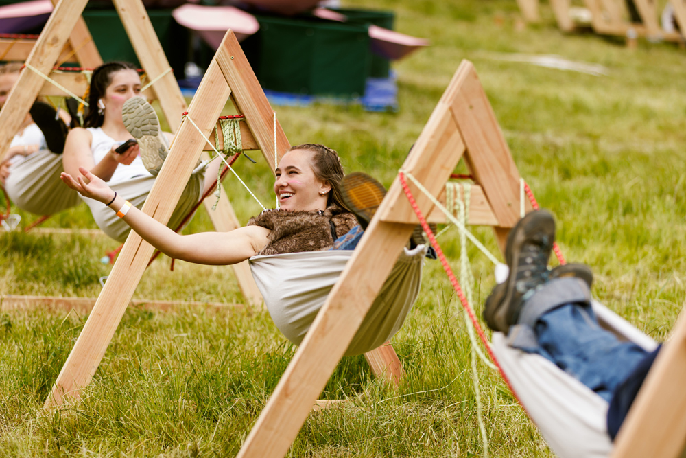 Students sit in hammocks held by triangular wooden structures during Design Village