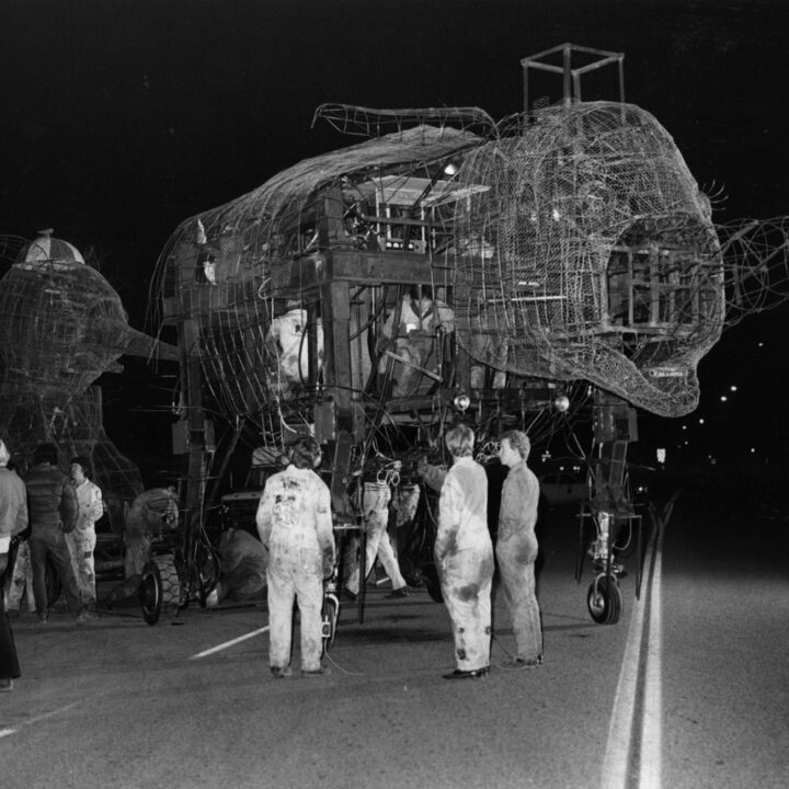 A black and white archive image of students in coveralls standing near a steel structure of a parade float in the shape of two elephants