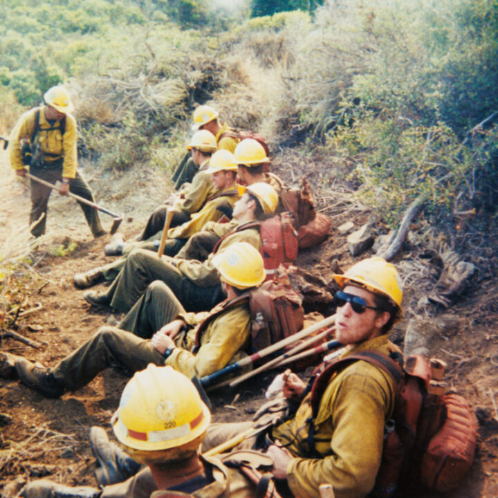 An archive image of young firefighters wearing yellow helmets and jackets while sitting on a hillside.