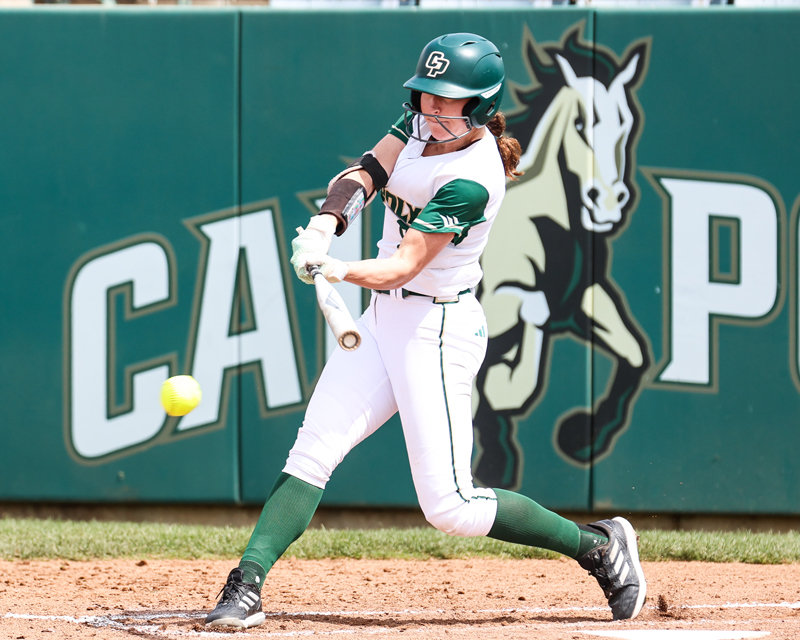 A Cal Poly softball player swings a bat in front of a university logo