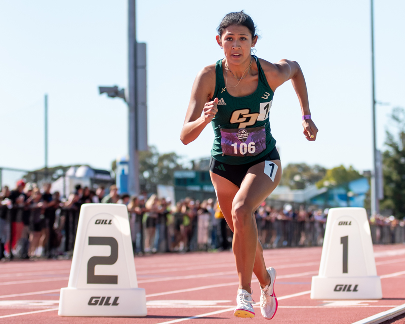 A women's track and field athlete runs near starting blocks on Cal Poly's track