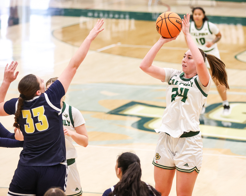 A Cal Poly women's basketball player shoots the ball over a competitor on a basketball court