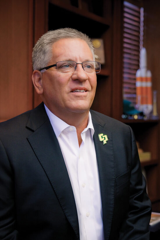 President Armstrong smiling in his office in a black suit and white shirt.