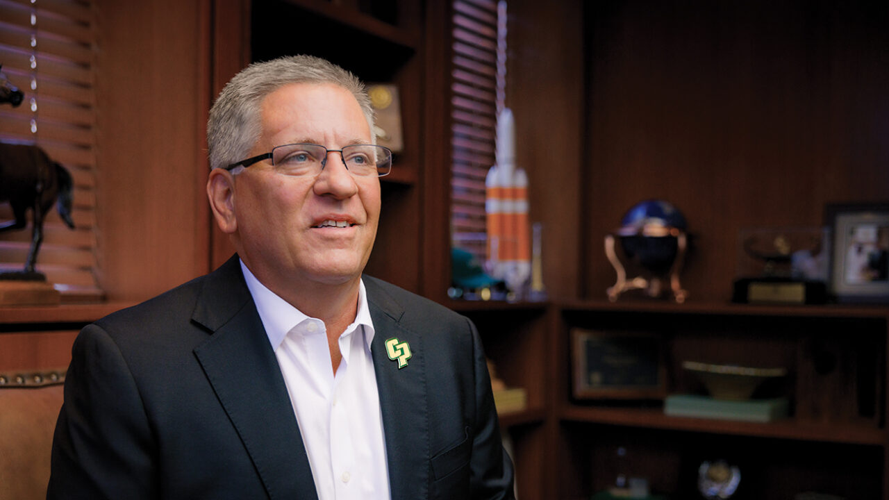 President Jeffrey Armstrong smiling in his office in a black suit and white shirt.