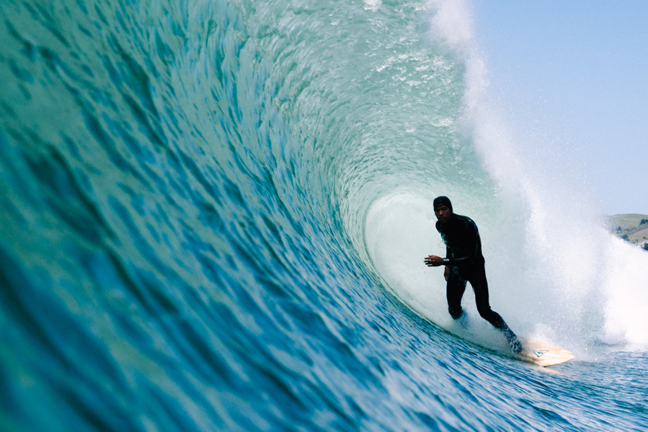 Alumnus Chad Jackson, in a wetsuit, surfs inside the tube of a wave.