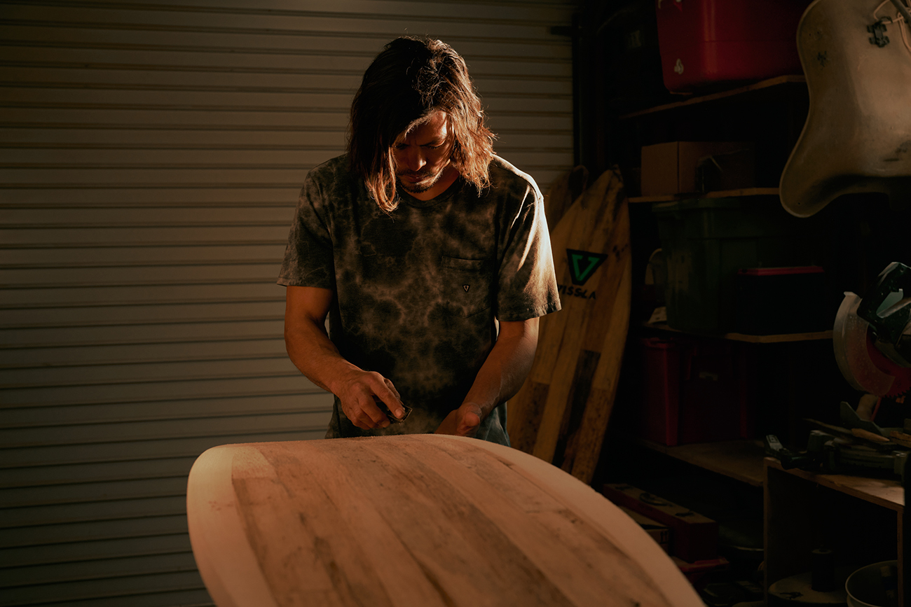 Jackson in a workshop using a tool to shape a board made from wood planks.