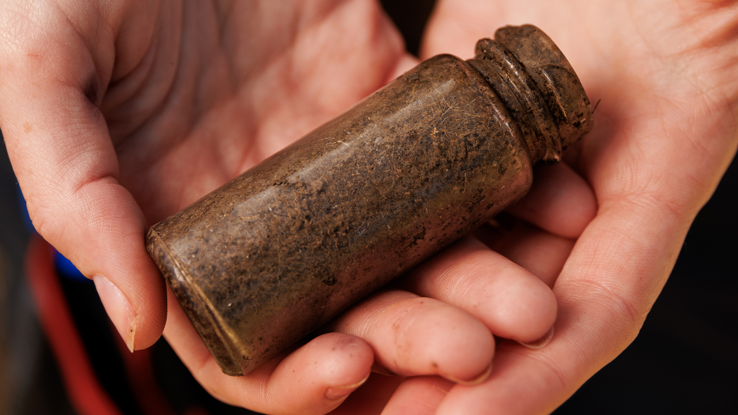 Two hands hold a dirt-covered glass bottle unearthed from an excavation