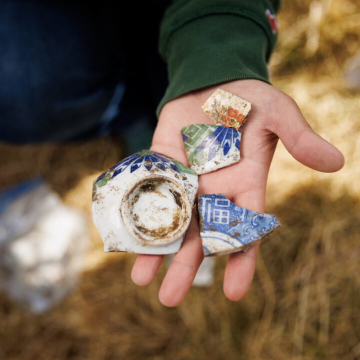 A hand holding four broken pieces of brightly colored Japanese pottery