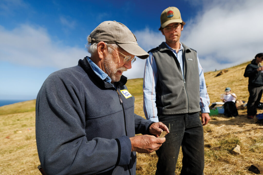 Two men wearing baseball caps look at an artifact from an anthropological dig