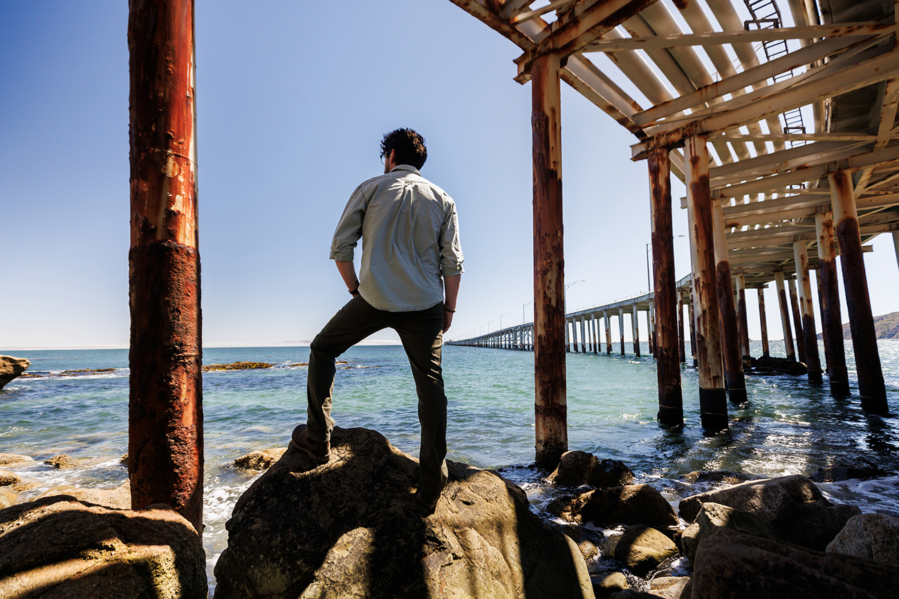 Editor Larry Peña stands on rocks overlooking the ocean at the Cal Poly Pier.