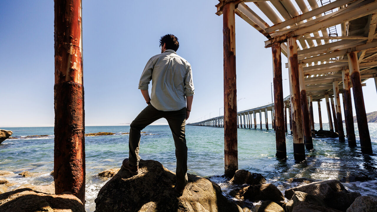 Editor Larry Peña stands on rocks overlooking the ocean at the Cal Poly Pier.