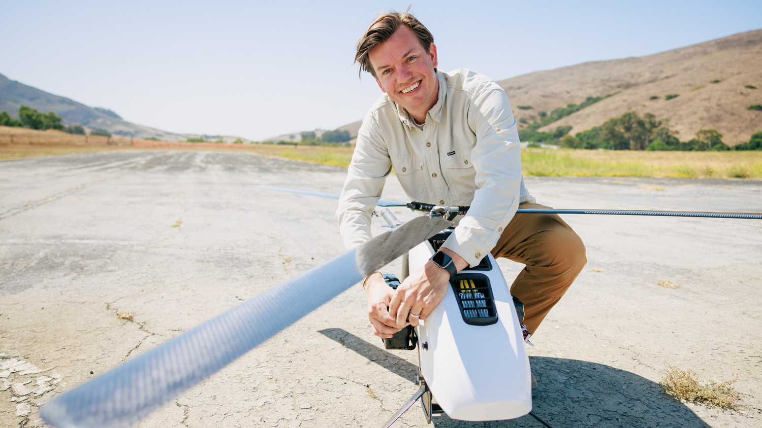 A person smiles while tending to a drone on a vacant runway