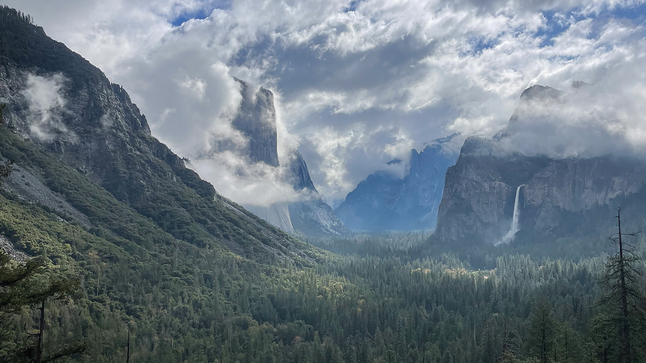 A forest-filled valley bounded by mountain peaks, with dramatic clouds drifting above.