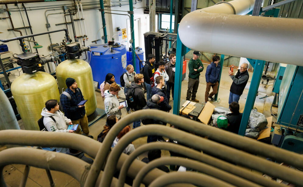 Students and a faculty member tour a power plant facility with large boilers, pipes and equipment.