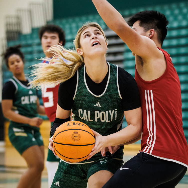 A women's basketball player competes against members of a practice squad on the court