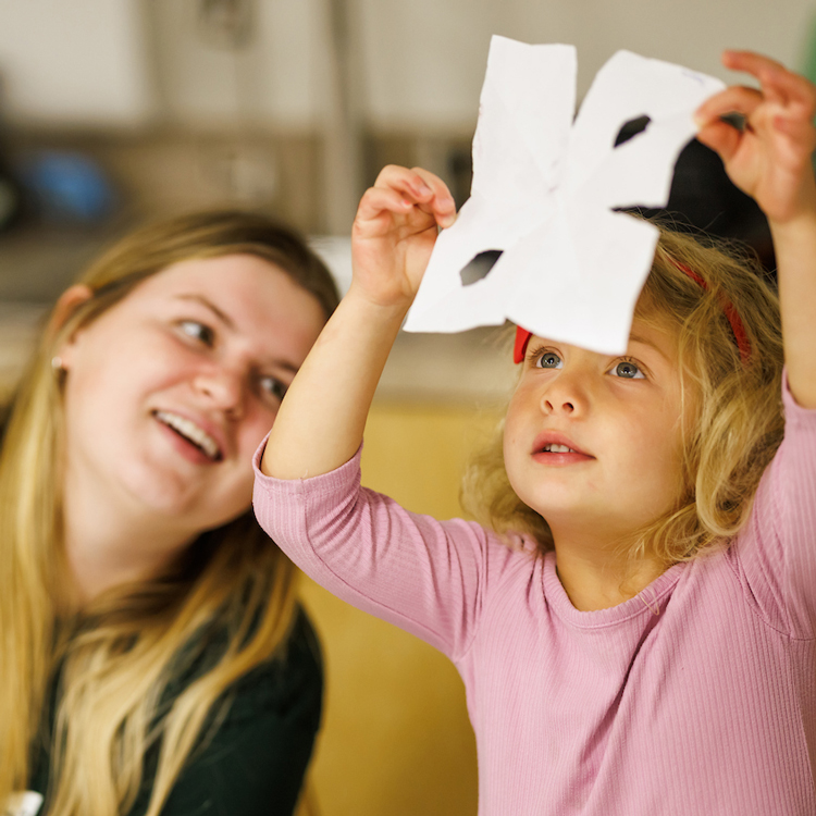 A student watches as a child lifts up a white paper snowflake craft