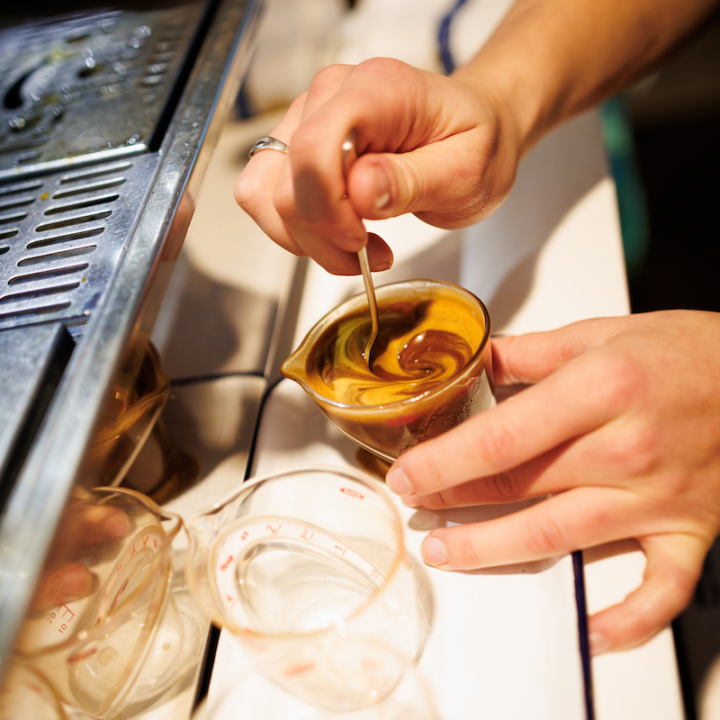 The hands of a student swirling a spoon into a coffee drink