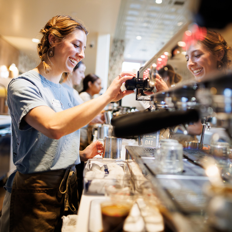 A student employee smiles while working behind the counter at a coffee shop