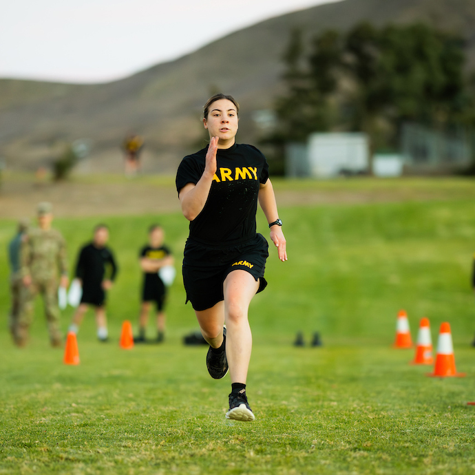 An ROTC cadet wearing a black Army t-shirt runs between orange cones on grass