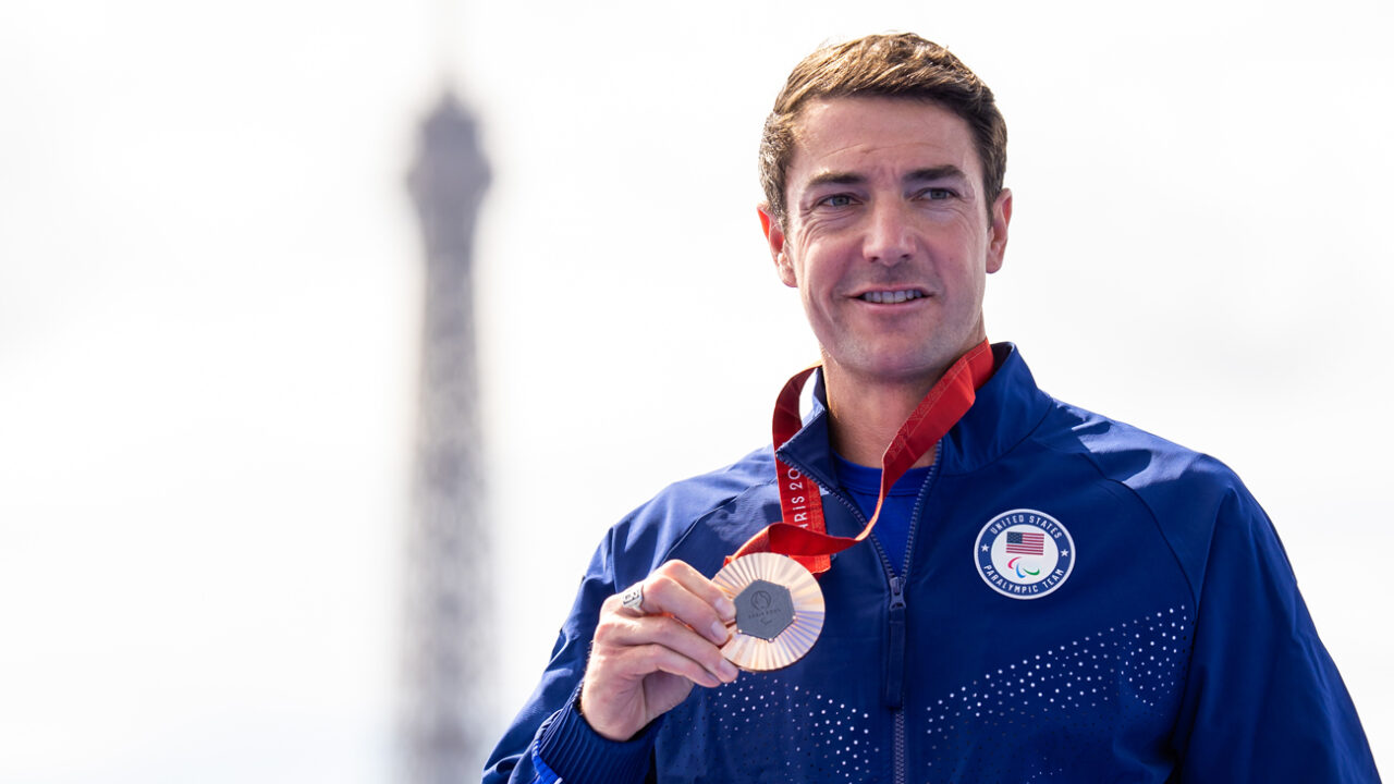 Mark Barr holds a bronze medal while wearing a blue Team USA jacket in front of the Eiffel Tower