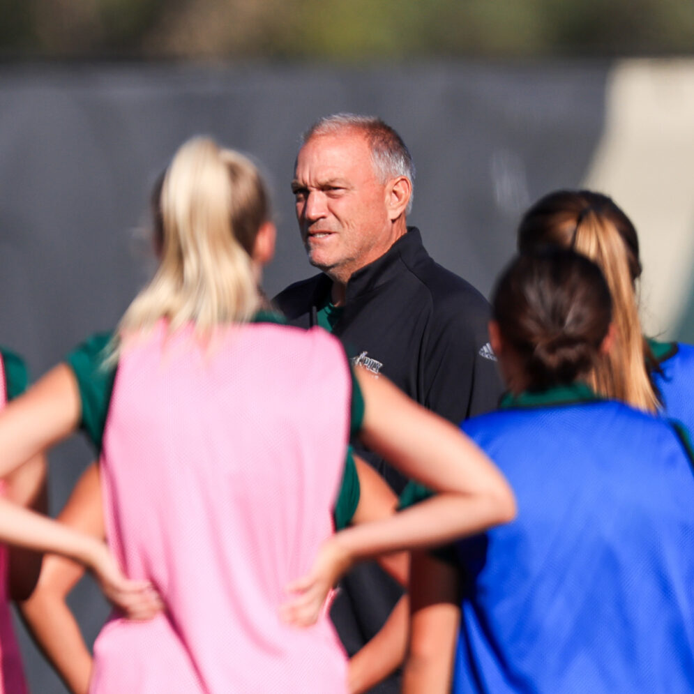 Women's soccer head coach Alex Crozier stands among his players and gives instructions