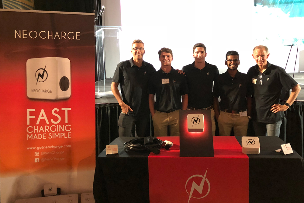 Five members of the NeoCharge team stand at the company's branded booth at Demo Day 2018 in the Fremont Theater