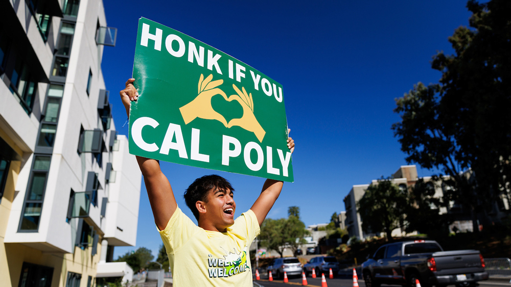 A student holds a sign that says 'Honk if you love Cal Poly'