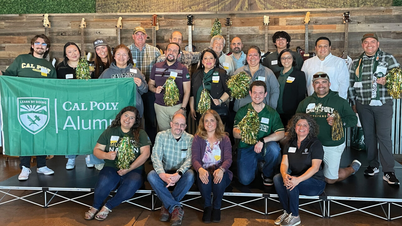Dozens of Cal Poly alumni from the Latinx Alumni Network smile next to a green flag