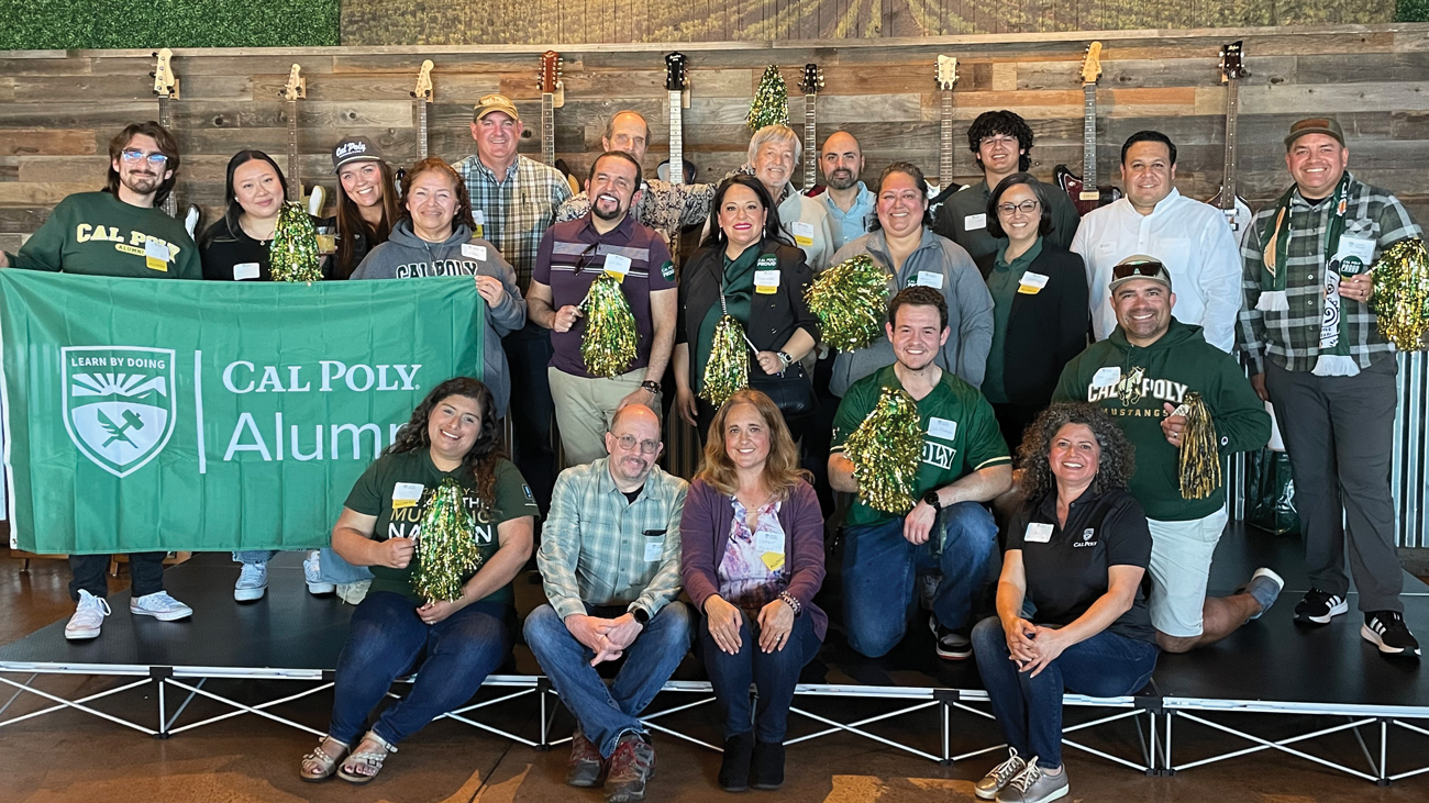 Dozens of Cal Poly alumni from the Latinx Alumni Network smile next to a green flag