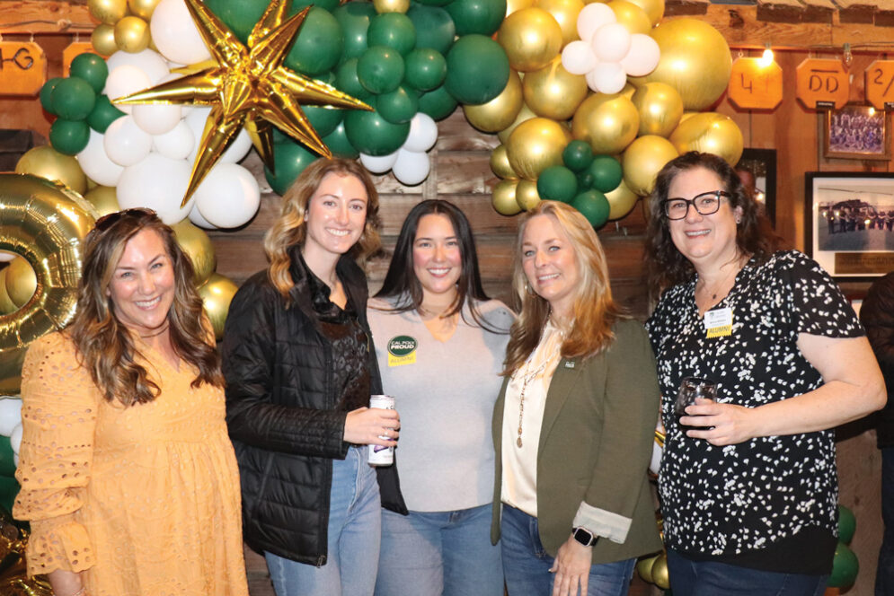 Five alumni from the Cal Poly Modesto Network smile near green and gold balloons