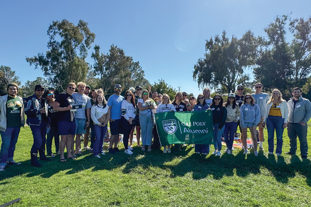 Dozens of Cal Poly alumni smile on a green hillside at an event for the Cal Poly San Diego Alumni Network