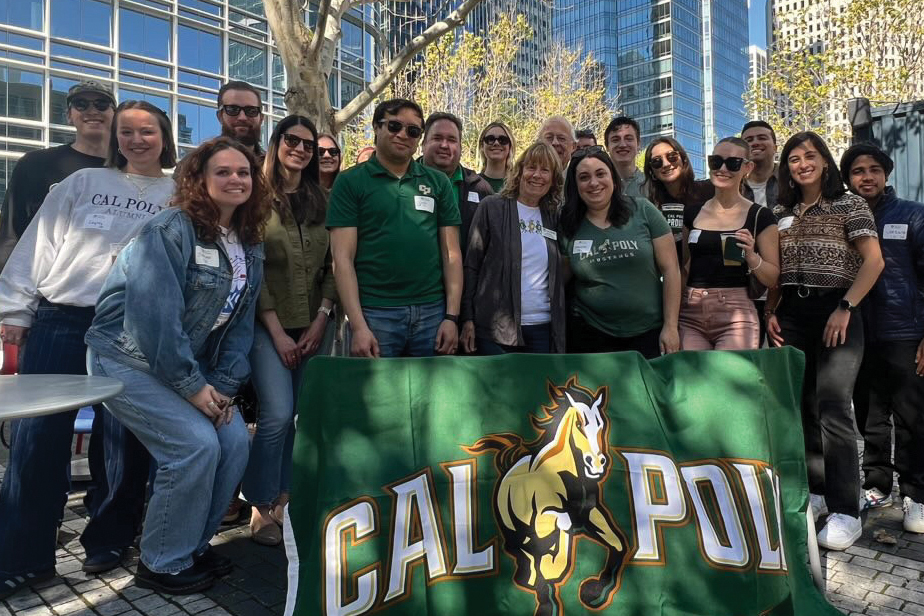 Cal Poly alumni smile near a Cal Poly flag in San Francisco