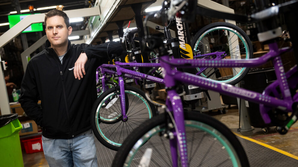 CEO Brian Riley stands next to a rack of purple bicycles