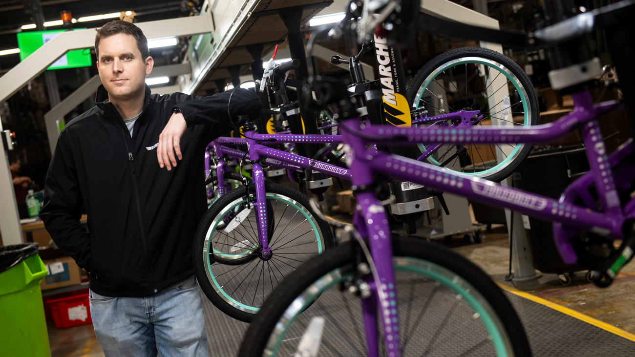 CEO Brian Riley stands next to a rack of purple bicycles