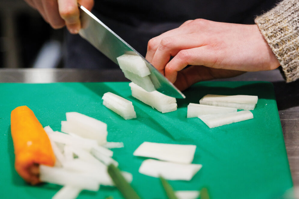 A student uses a knife to chop vegetables on a green cutting board