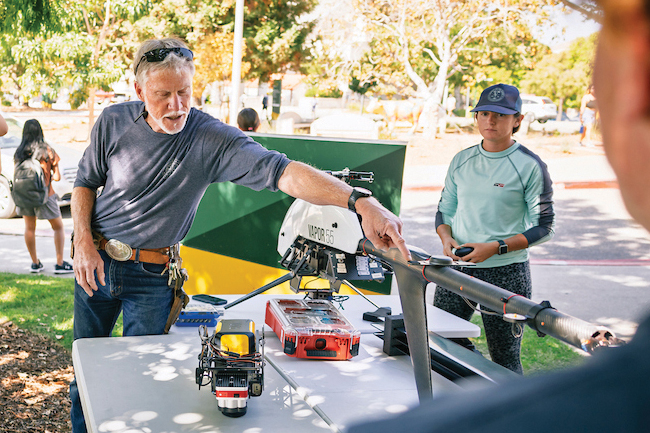 A faculty member touches the edge of a drone system as students look on