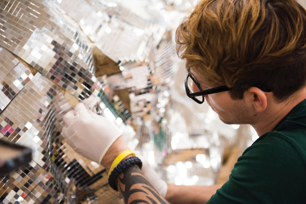 A student applies silver sequins to an art installation