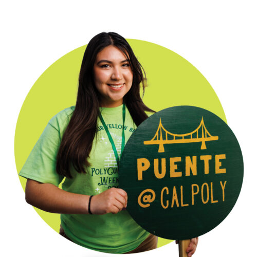 Denis Gonzalez-Reyes smiles while holding a green sign that reads Puente @ Cal Poly