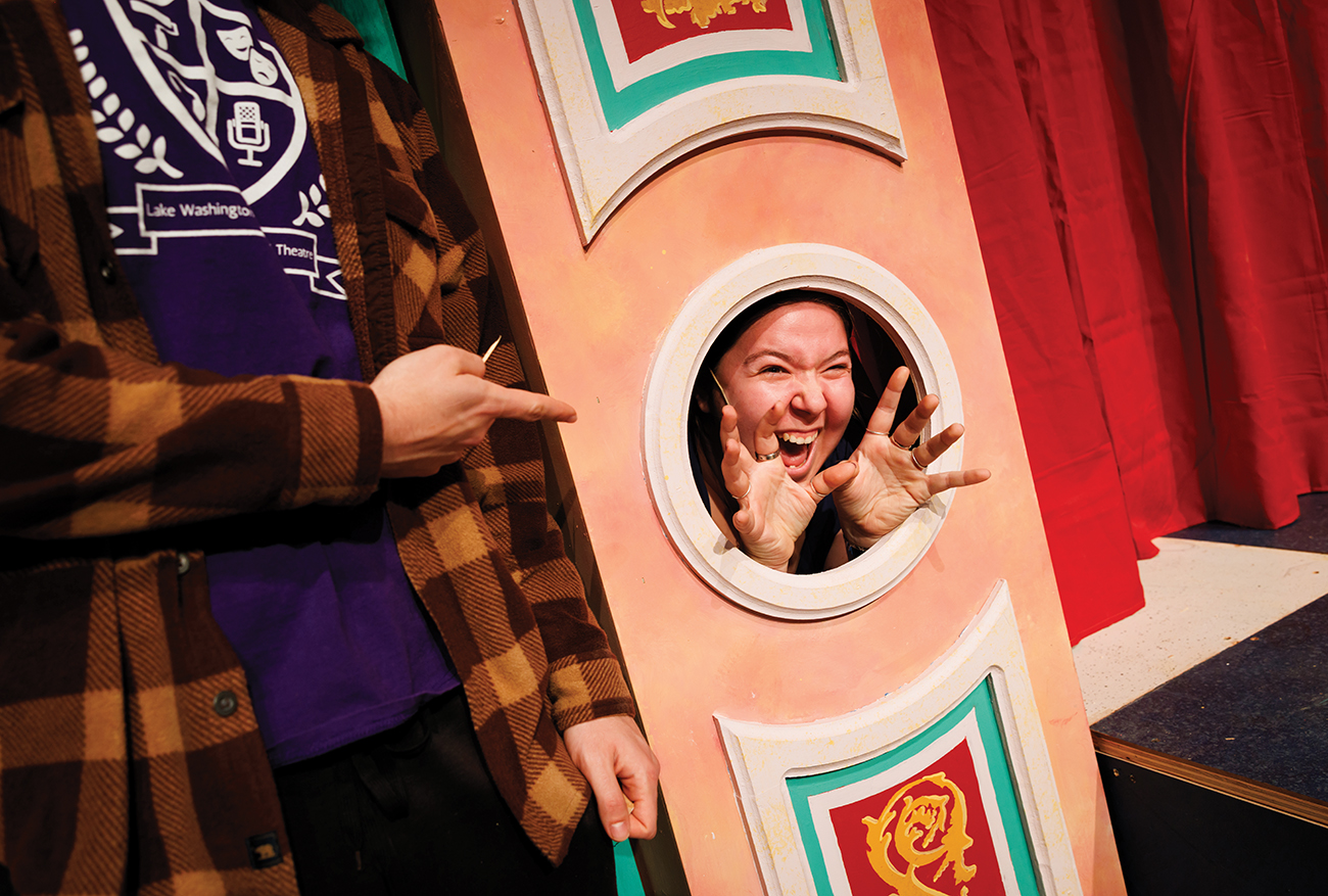 A young woman pokes her face and hands through a round cutout in an elaborately-decorated pink pillar.