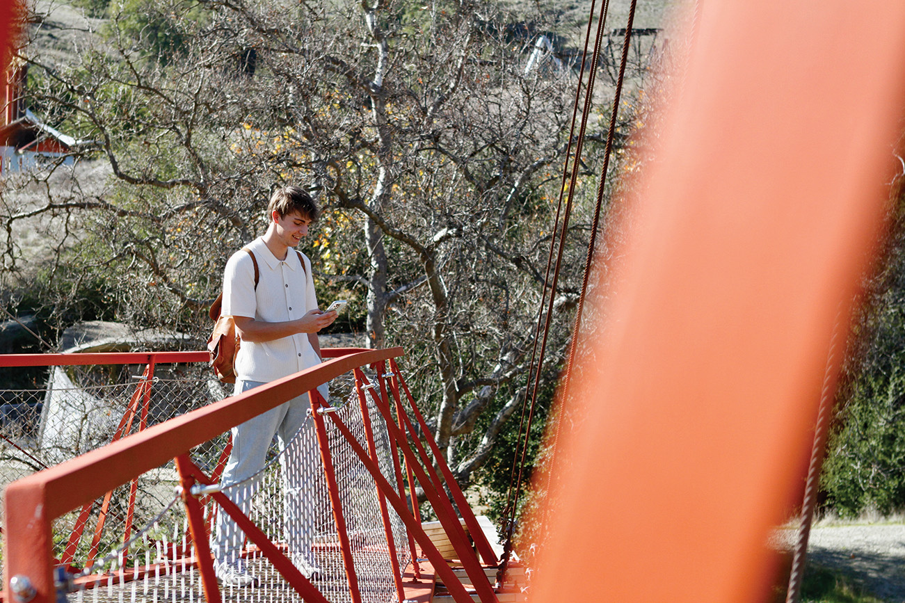 A young man holds a mobile phone while walking on a platform surrounded by an orange railing.