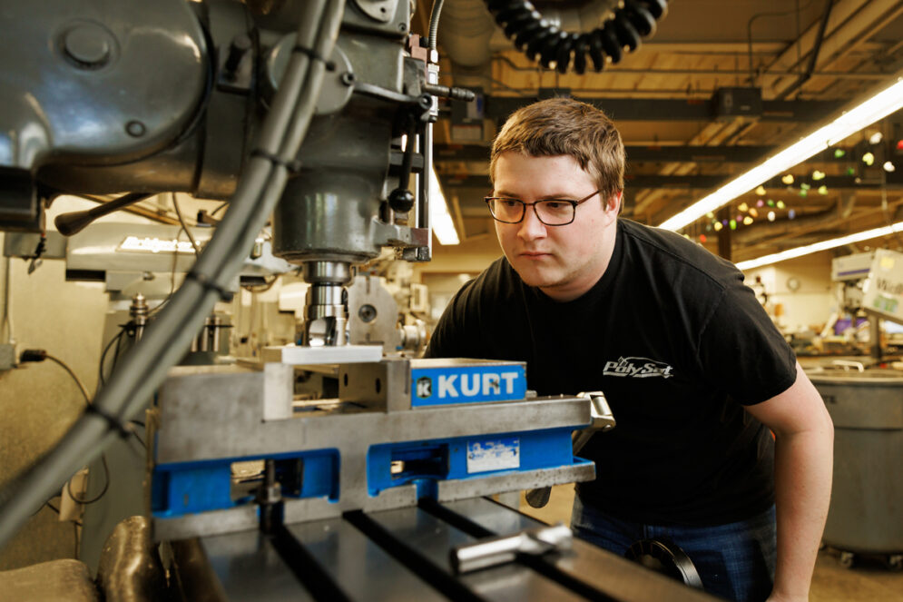 A student looks closely at a machining tool in a machine shop