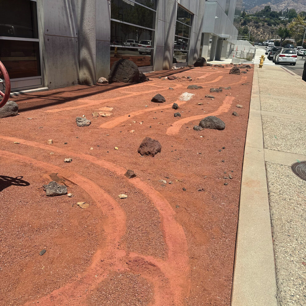 The Mars-inspired art installation with red dirt, rover tracks and rocks, outside the Flight Electronics Integration Facility at Jet Propulsion Laboratory
