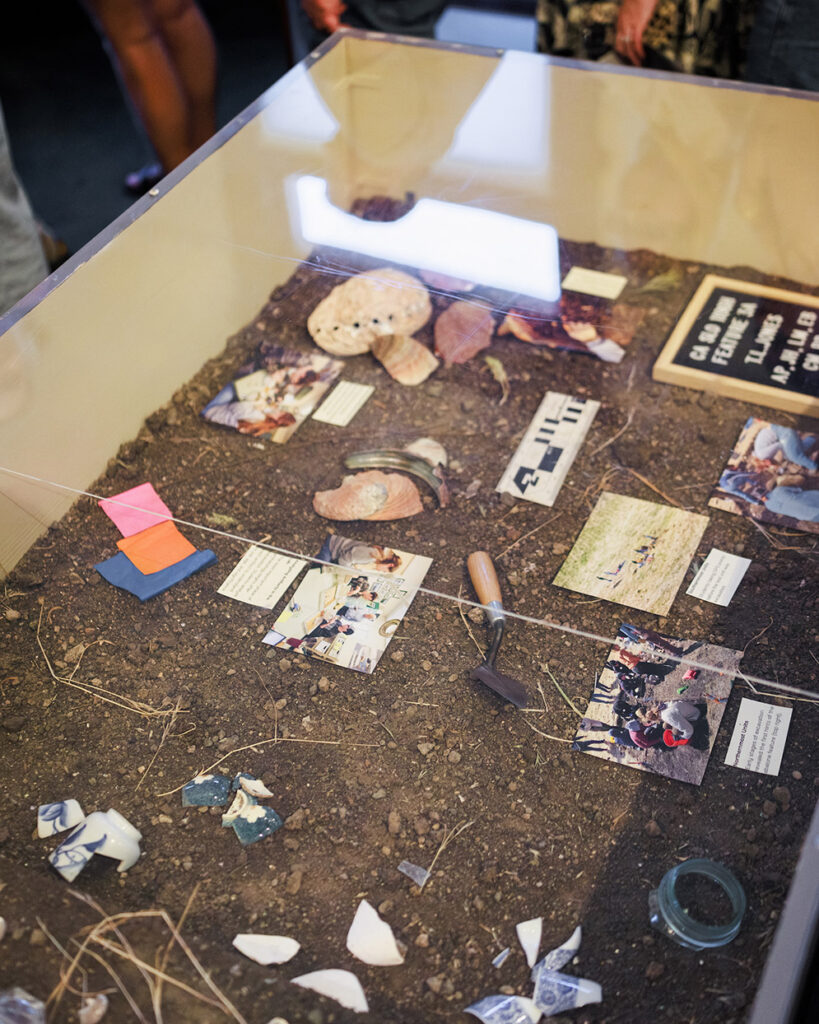 A collection of artifacts from the Yoshida homestead on top of soil in an exhibit case.