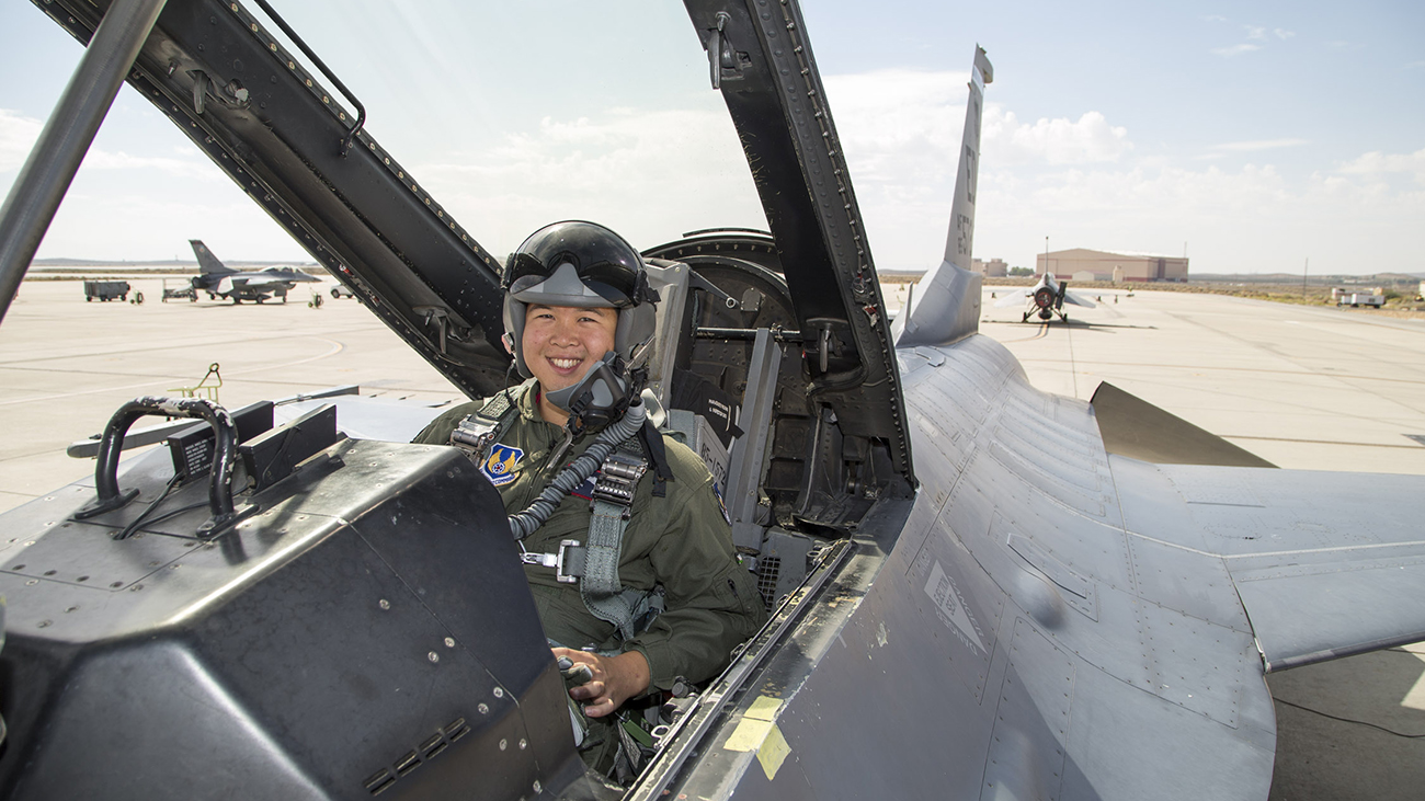 A young man in military gear smiles in the cockpit of a fighter jet.