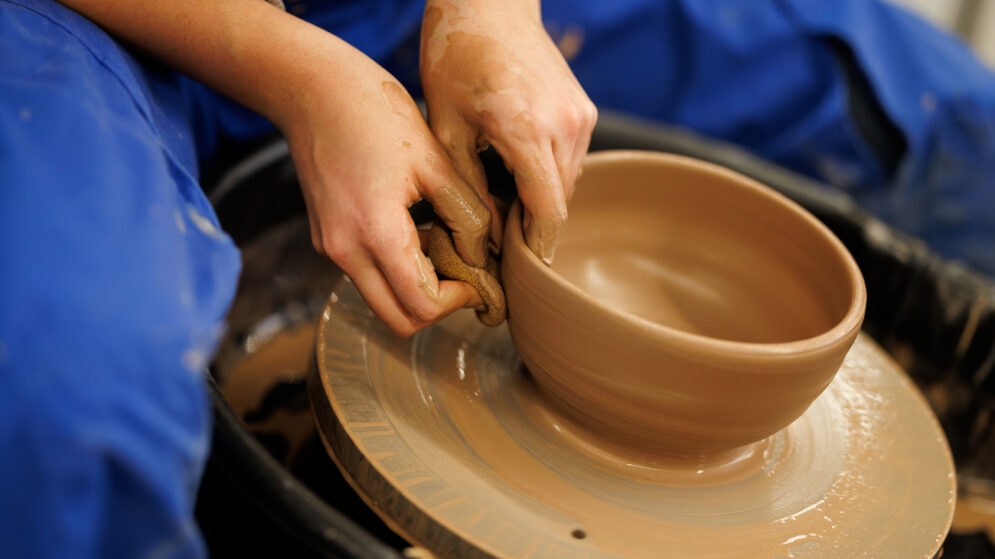 A student shapes a bowl on a pottery wheel