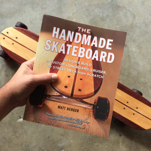 A person holds a book above a handmade skateboard