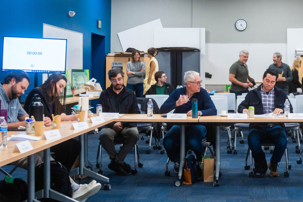 More than ten alumni of different ages work at tables in a blue classroom during an Innovation Quest event