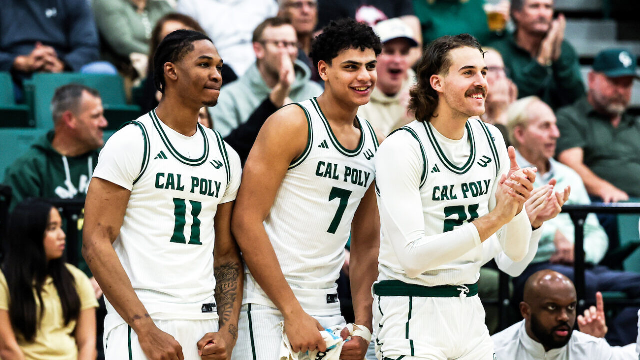 Three Cal Poly men's basketball players cheer their teammates on from the sidelines