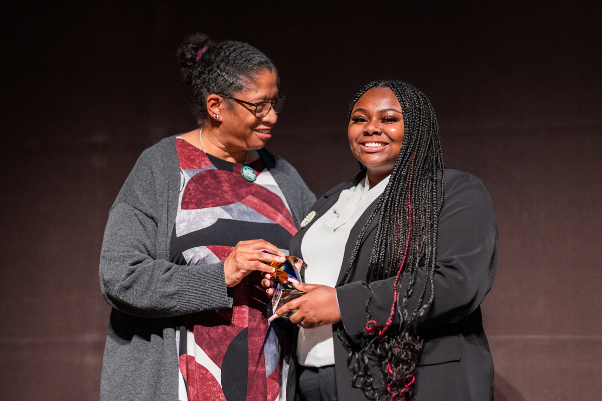 A faculty member presents a glass award statue to a student at Cal Poly