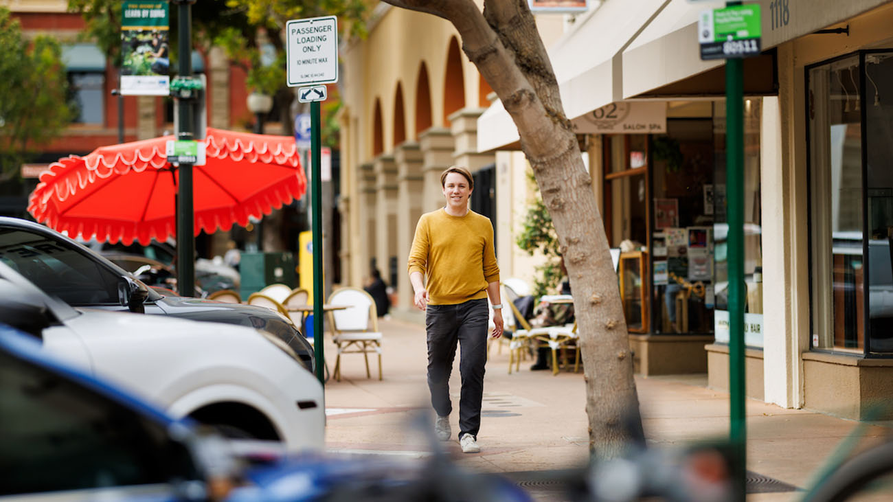 A man in a yellow sweater walks across a downtown plaza